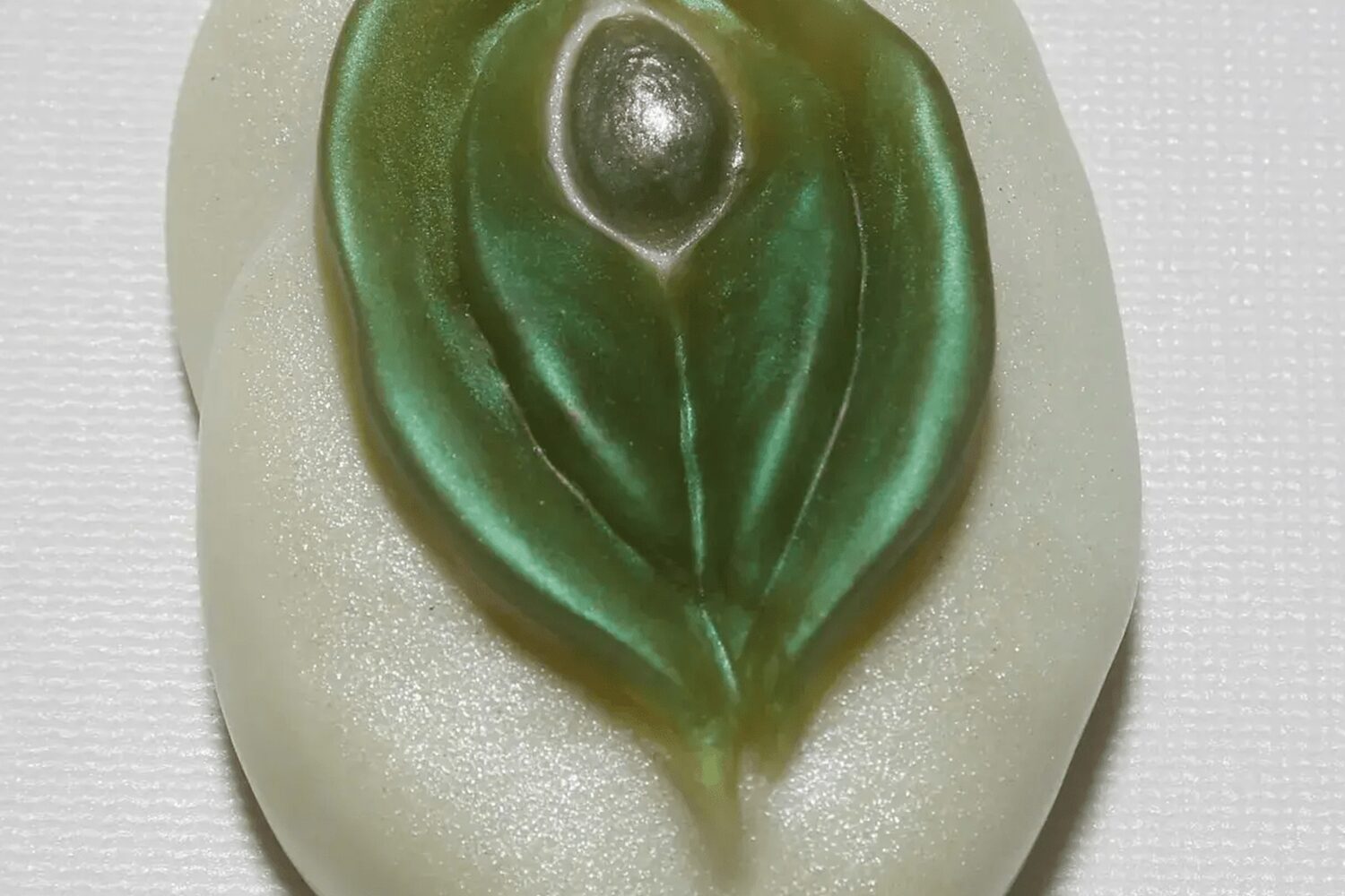 A green leaf shaped soap sitting on top of a white surface.