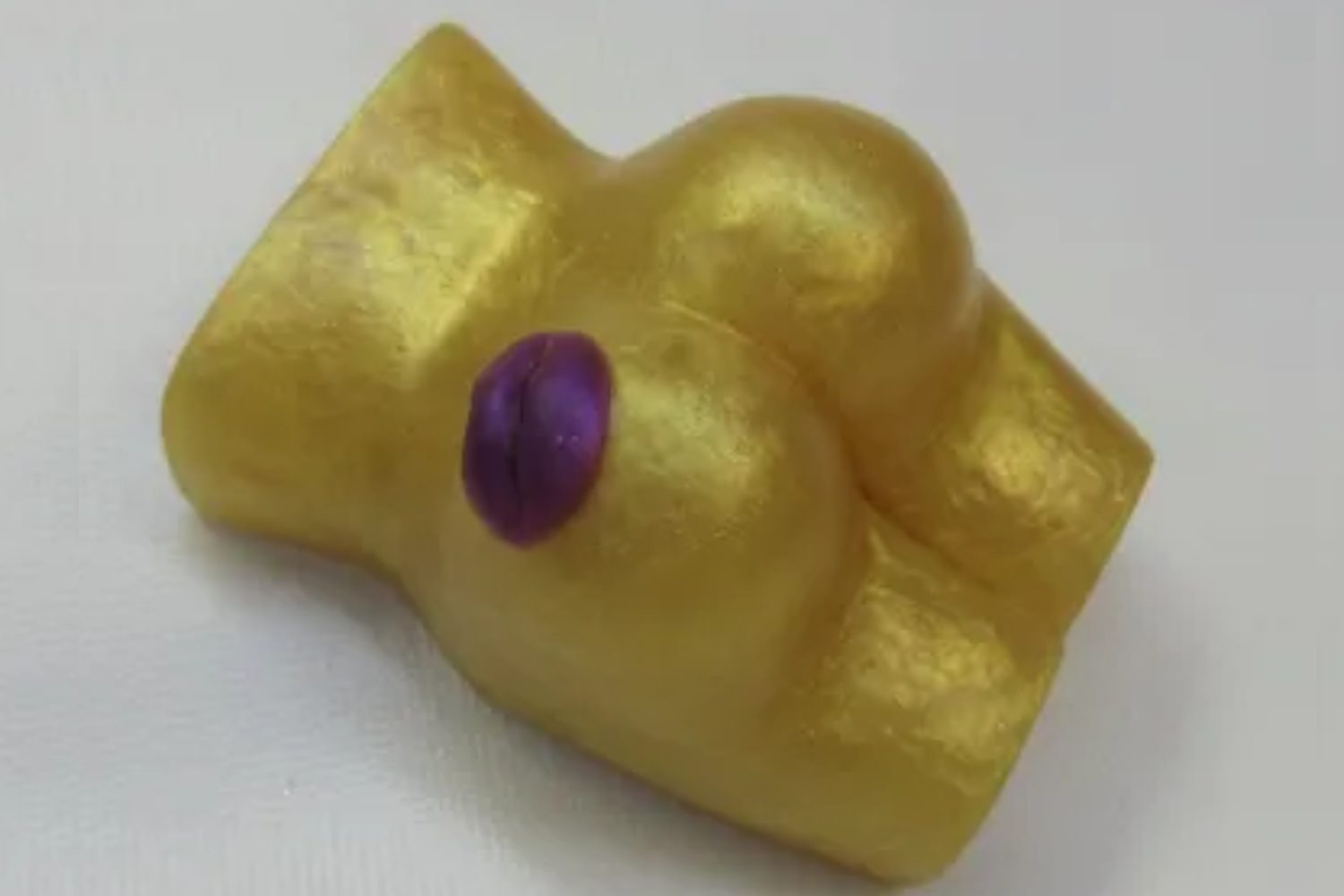 A gold colored object with purple eyes and a large breast.