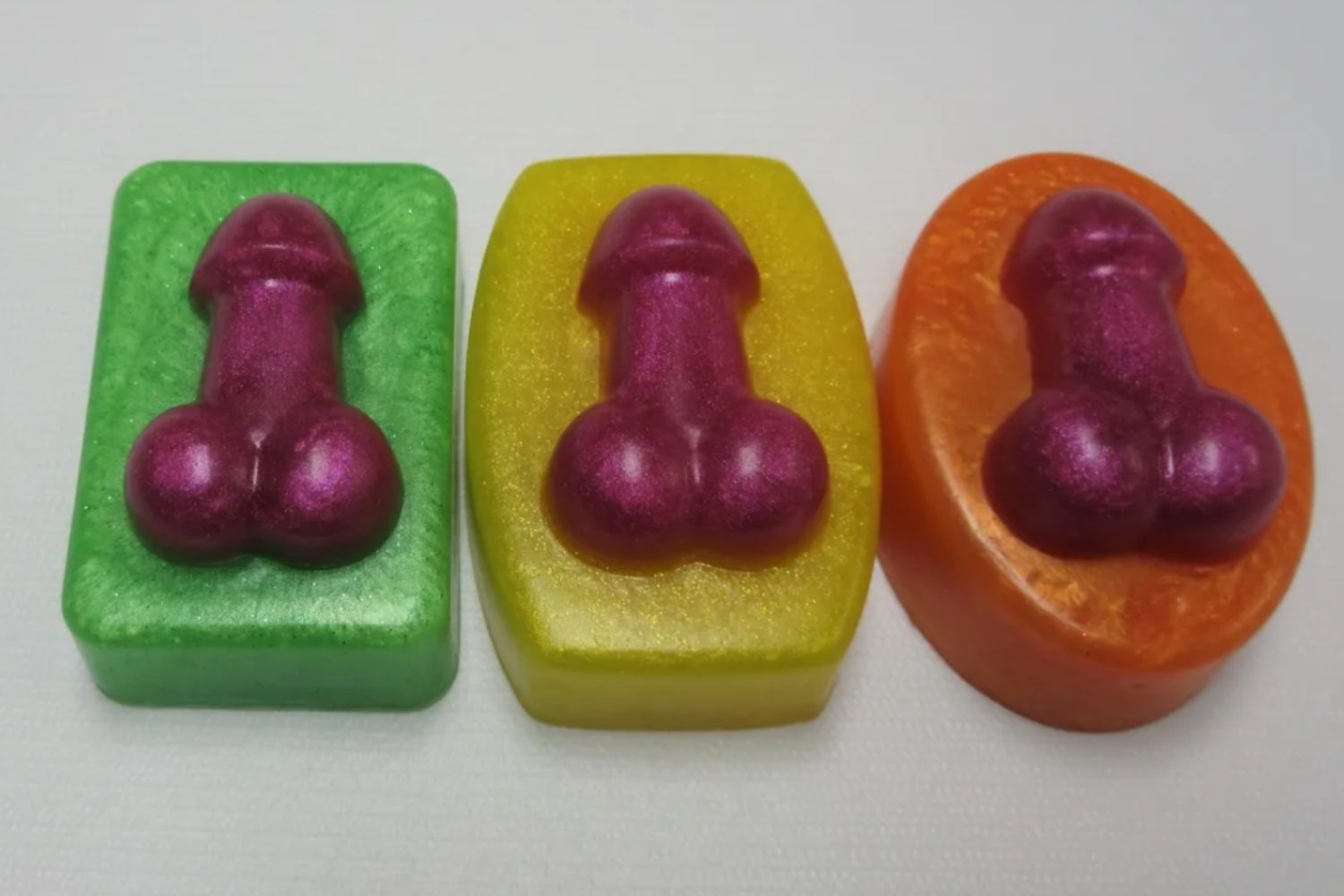 Three different colored soaps with a purple condom on top of them.
