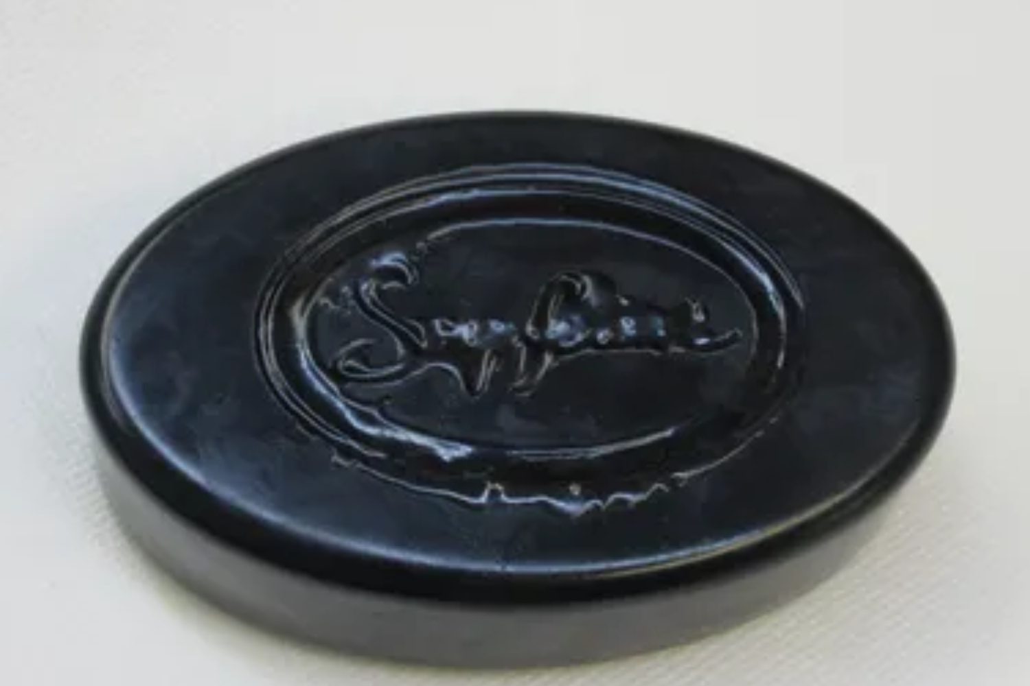 A black round soap dish with the word soapy on it.