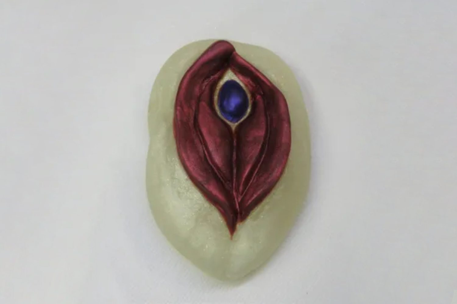 A white stone with a red leaf and blue bead on it.