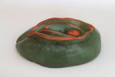 A green and red clay sculpture on top of white surface.